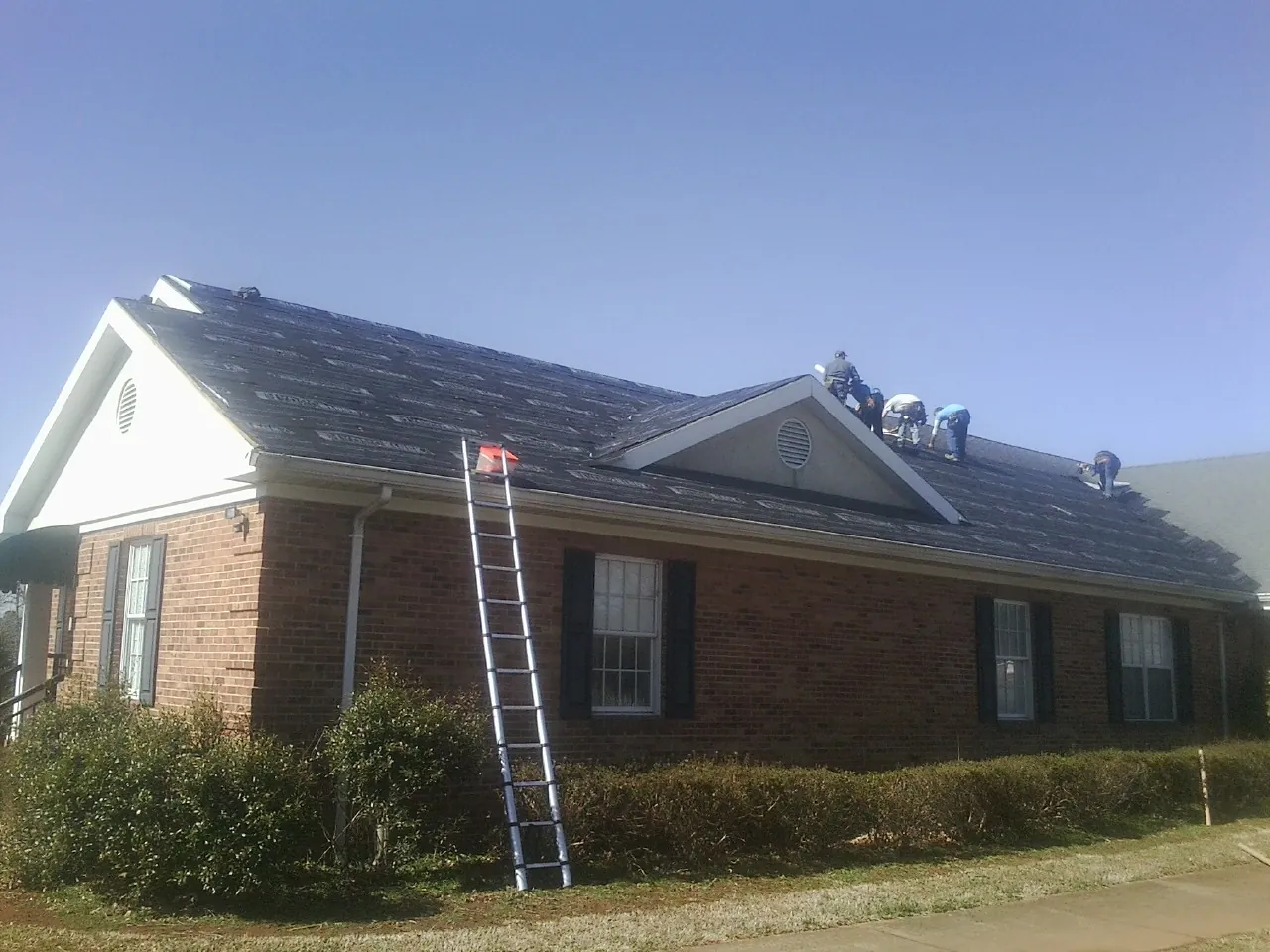 Crew tearing shingles off a brick ranch roof with a ladder set — Metal Roof Repair work by our crew in Ione