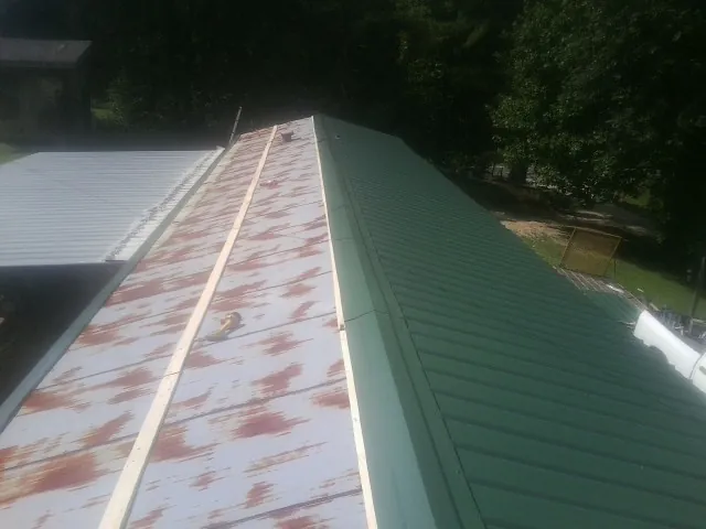 Old rusted panels beside newly installed green metal roofing in Ione