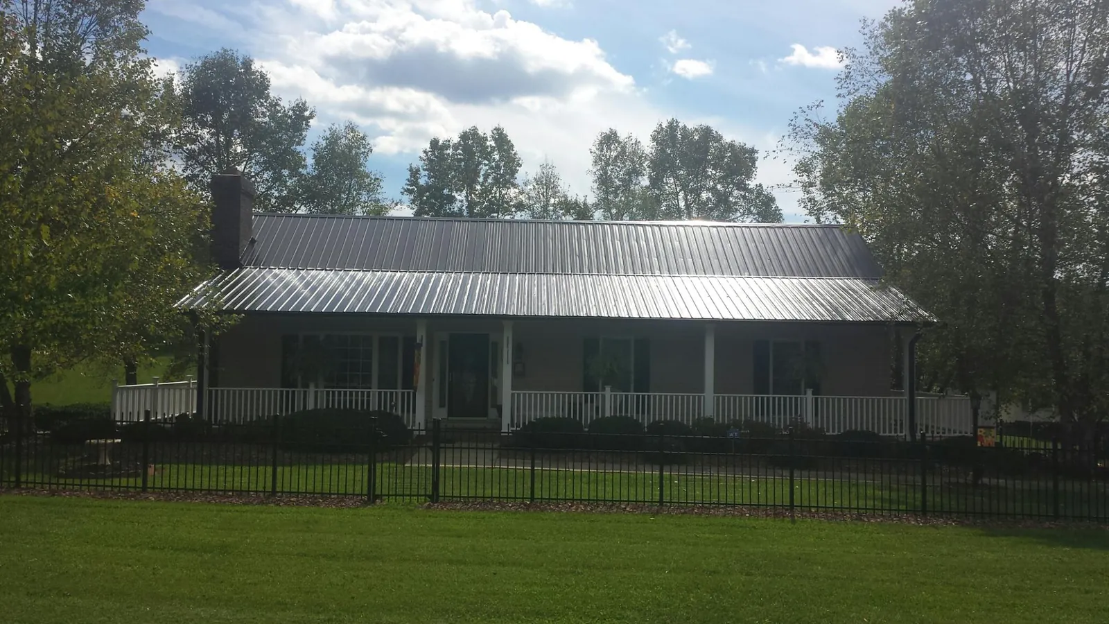Gray metal roof on a brick ranch with a full width front porch — Gutter Guard Installation work by our crew in Ione