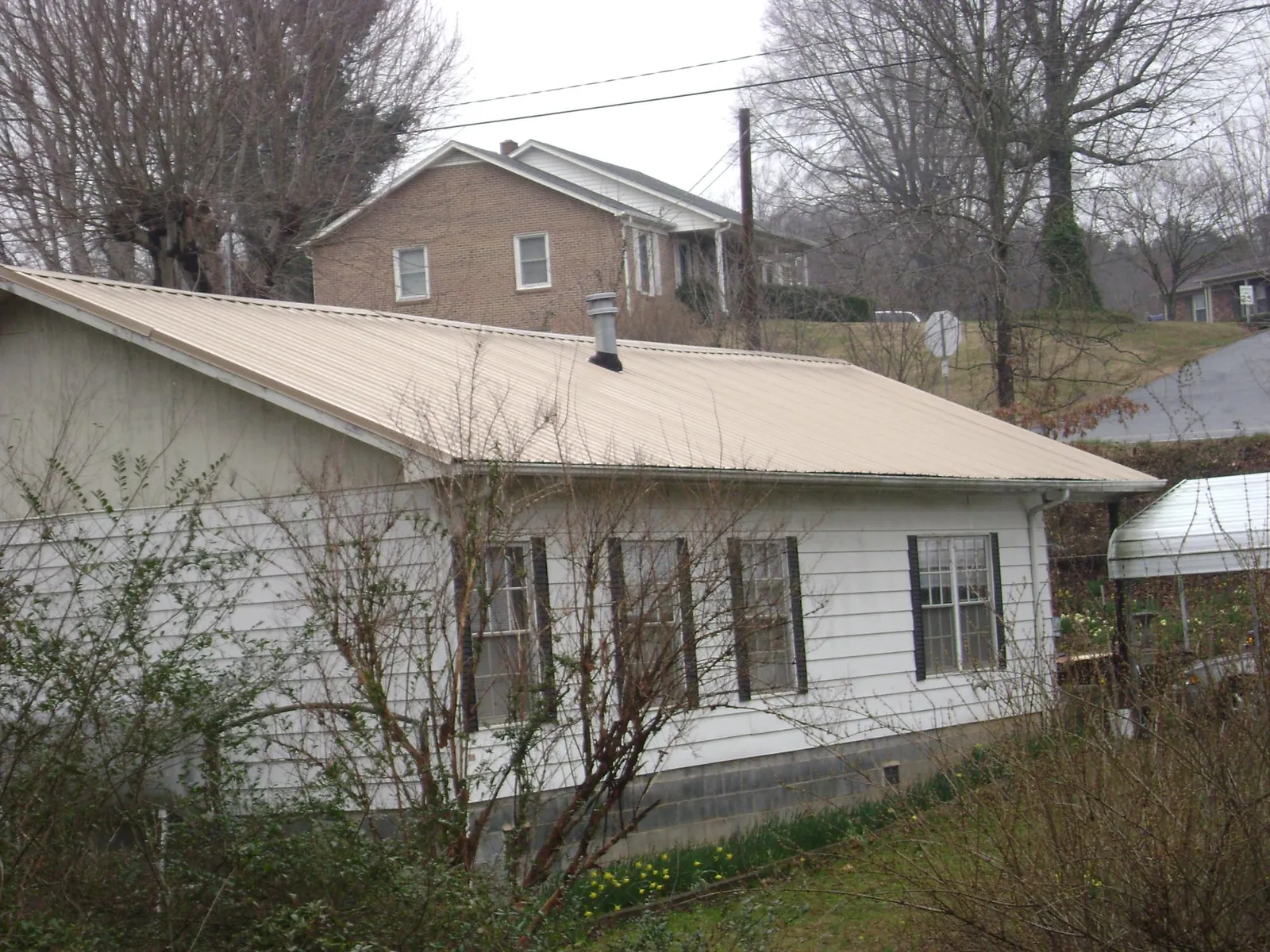 Tan metal roof on a white sided house set into a hillside — Commercial Roofing by Roofing Brothers in Ione